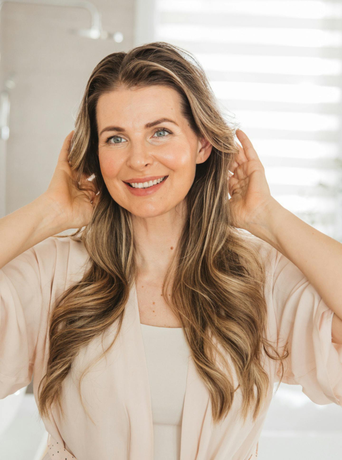 smiling female holds hands toward head and hair
