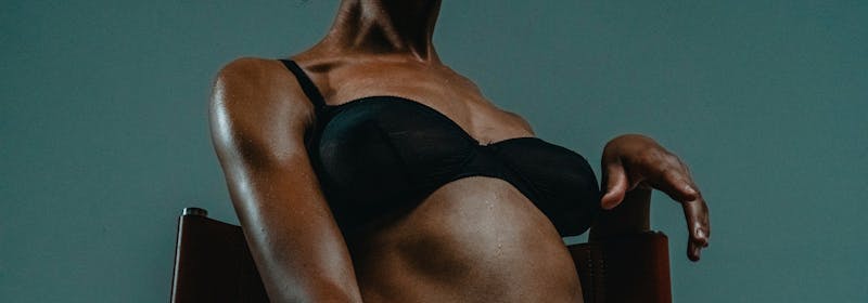 a woman sits back, perched hand, wearing bra