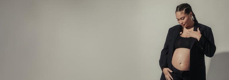 new mother, smiling, looks down at her abdomen, stretch marks visible