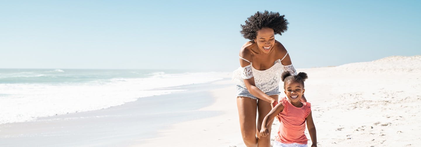 Smiling mother and daughter run together on beach