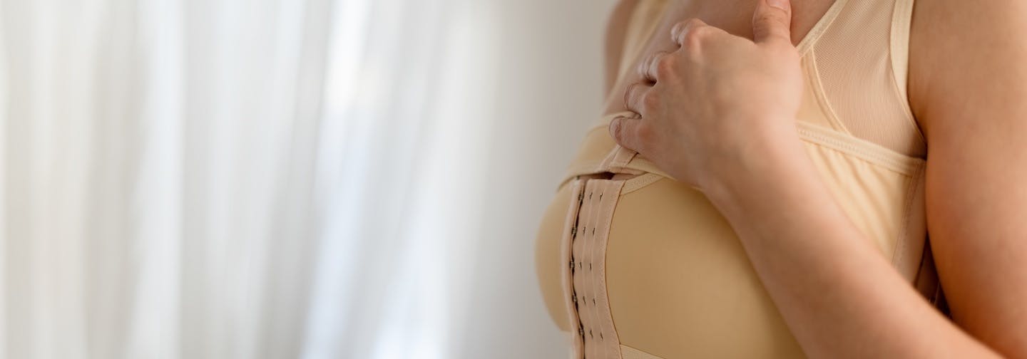 woman with post-op breast compression binder holds hand on chest