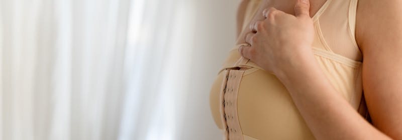 woman with post-op breast compression binder holds hand on chest