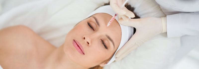 aerial view, gloved hands hold neuromodulator near woman's forehead