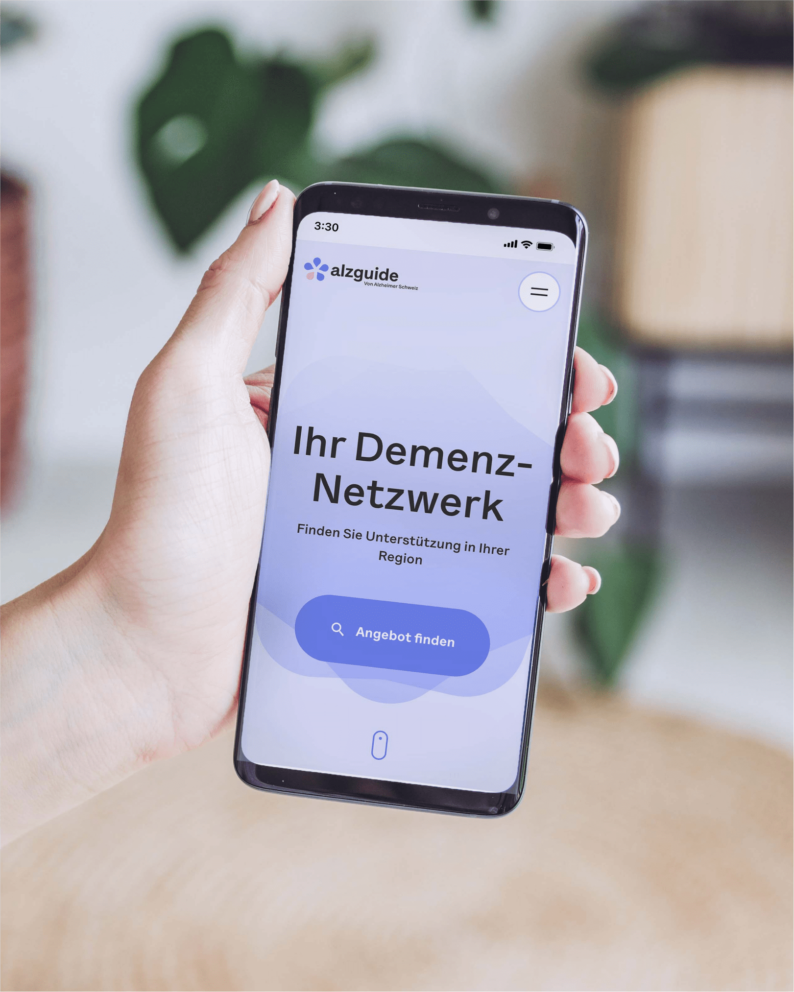 A hand holding a smartphone displaying the alzguide.ch homepage.