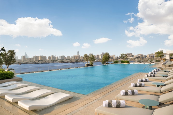 A luxurious infinity pool surrounded by sun loungers with rolled towels, overlooking a city skyline under a partly cloudy sky, creating a tranquil atmosphere for relaxation