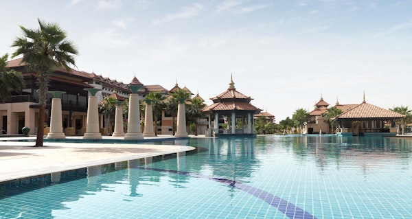 Large resort pool with traditional pavilion architecture and palm trees.