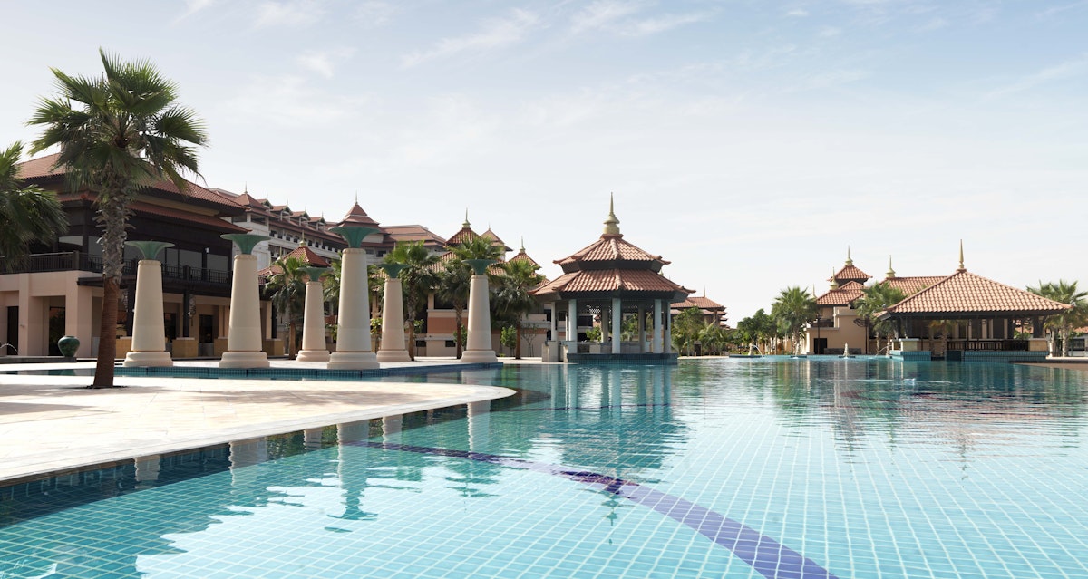 Large resort pool with traditional pavilion architecture and palm trees.