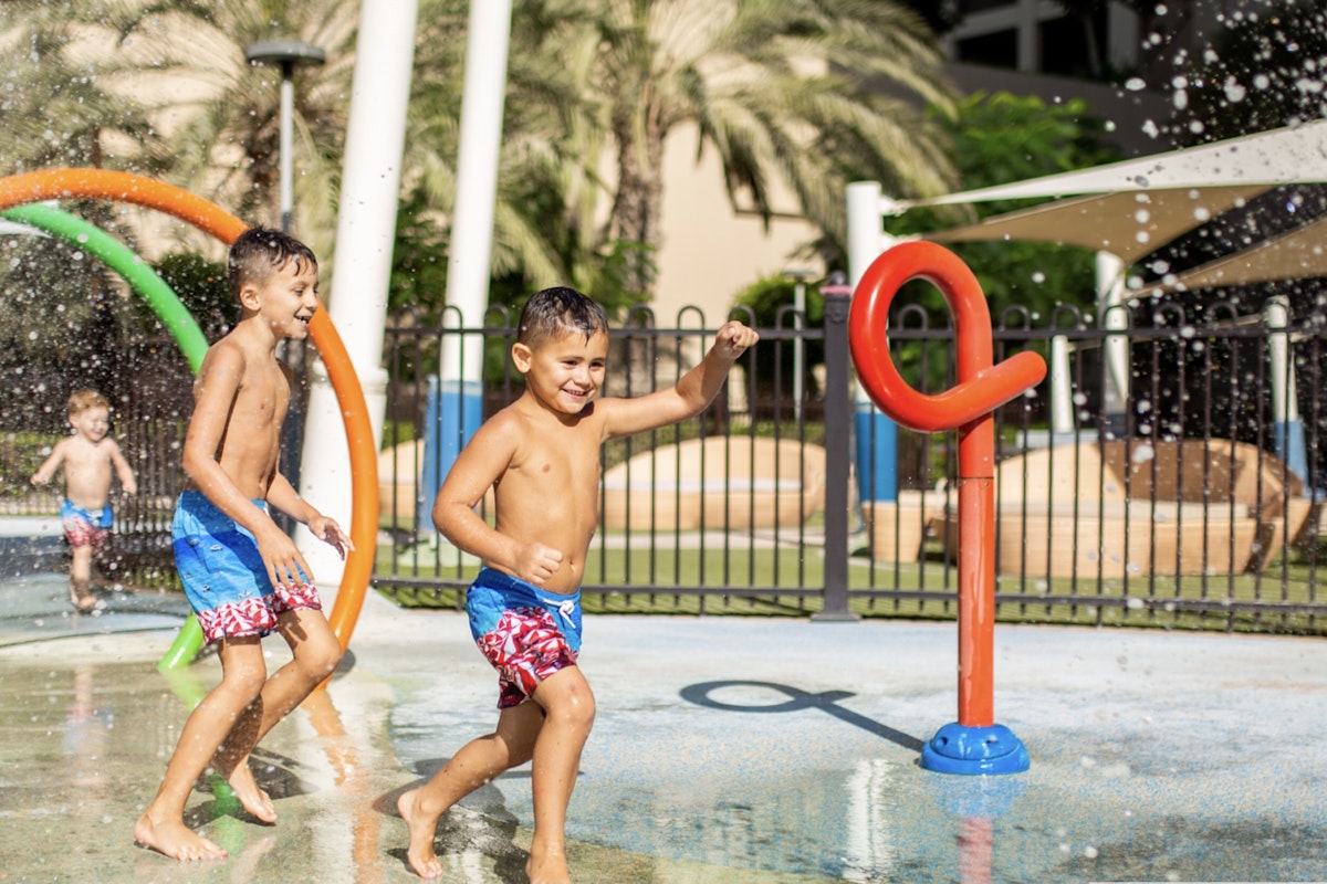 Fairmont The Palm Children playing in a water park with colorful spray features.