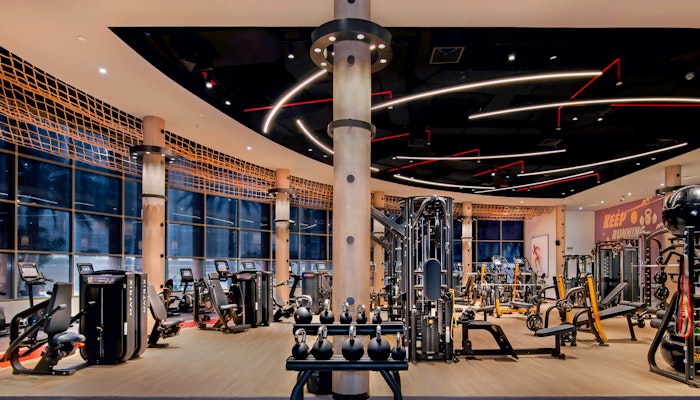 Sheraton Abu Dhabi Hotel & Resort Contemporary gym interior featuring a variety of exercise machines, weight racks, and unique ceiling lighting, creating a vibrant workout environment.