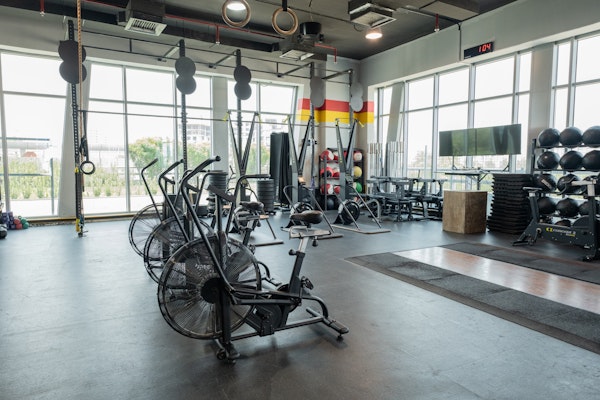 SK Fitness functional training area featuring air bikes, and free weights Spacious gym with large windows, featuring air bikes, CrossFit rings, and various workout equipment such as medicine balls, kettlebells, and resistance bands