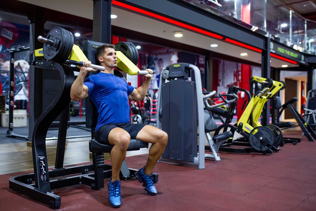 A man lifting weights on a machine in a modern gym setting.