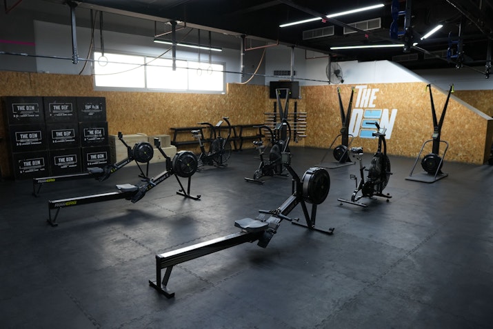 A gym featuring state-of-the-art equipment in a spacious training area with dark floors and the gym logo on the wall
