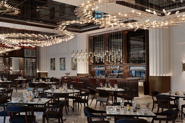 A sophisticated restaurant interior featuring luxurious chandeliers, dark wood furnishings, and beautifully set tables.