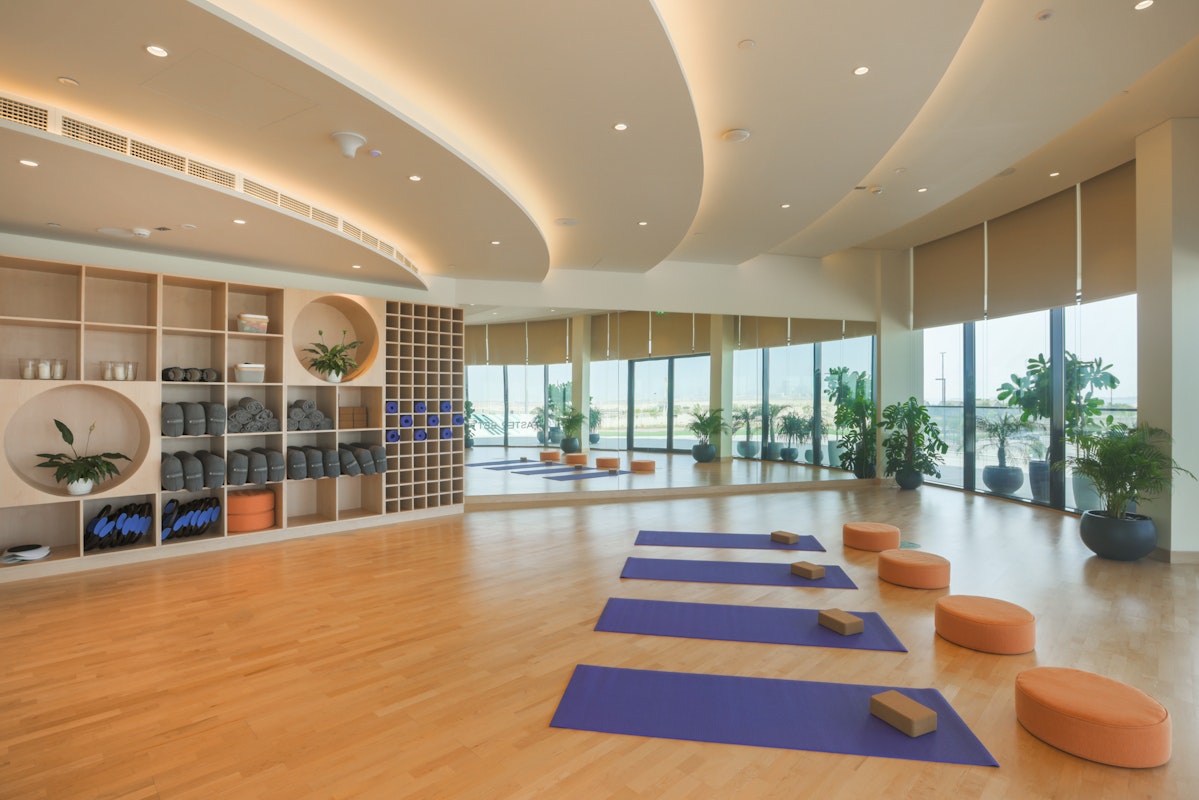 A spacious yoga studio with mats, blocks, and cushions, along with large windows offering a view of the outdoors.