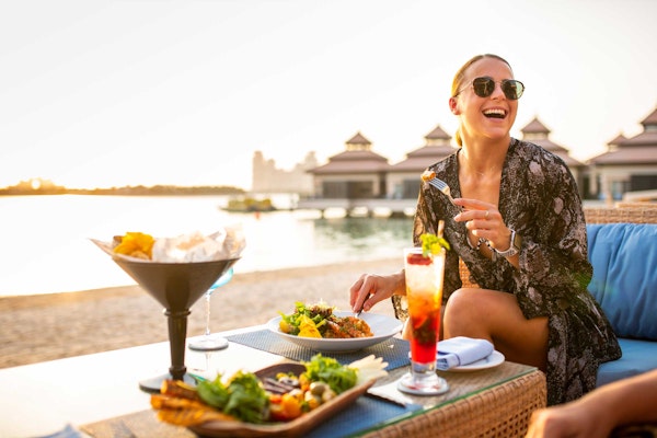 A woman enjoying a vibrant outdoor meal with cocktails and sunset