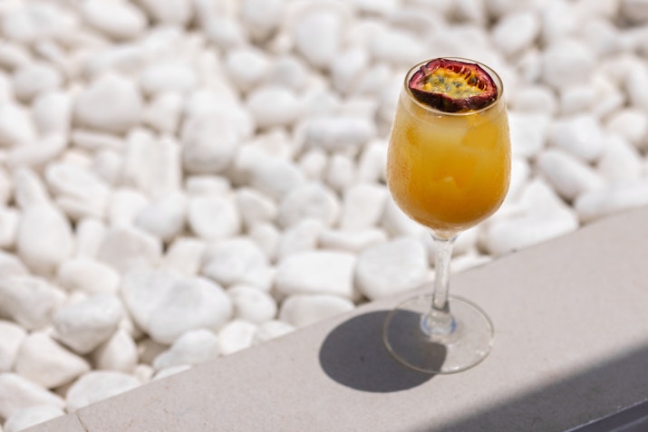 A glass of vibrant yellow cocktail garnished with dried fruit, resting on a light-colored surface next to white stones