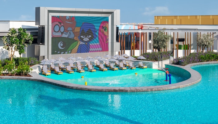 The WB, Abu Dhabi Outdoor pool area with lounge chairs and a large screen showing animated characters.