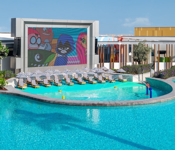 The WB, Abu Dhabi Outdoor pool area with lounge chairs and a large screen showing animated characters.