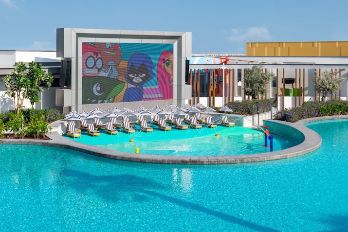 Outdoor pool area with lounge chairs and a large screen showing animated characters.