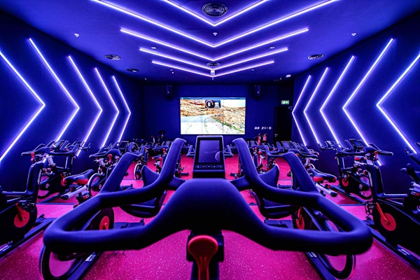 Focus on your Wellness Spinning room with exercise bikes, neon lighting, and a screen showing a cycling map