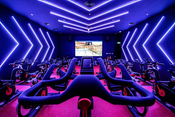 Focus on your Wellness Spinning room with exercise bikes, neon lighting, and a screen showing a cycling map