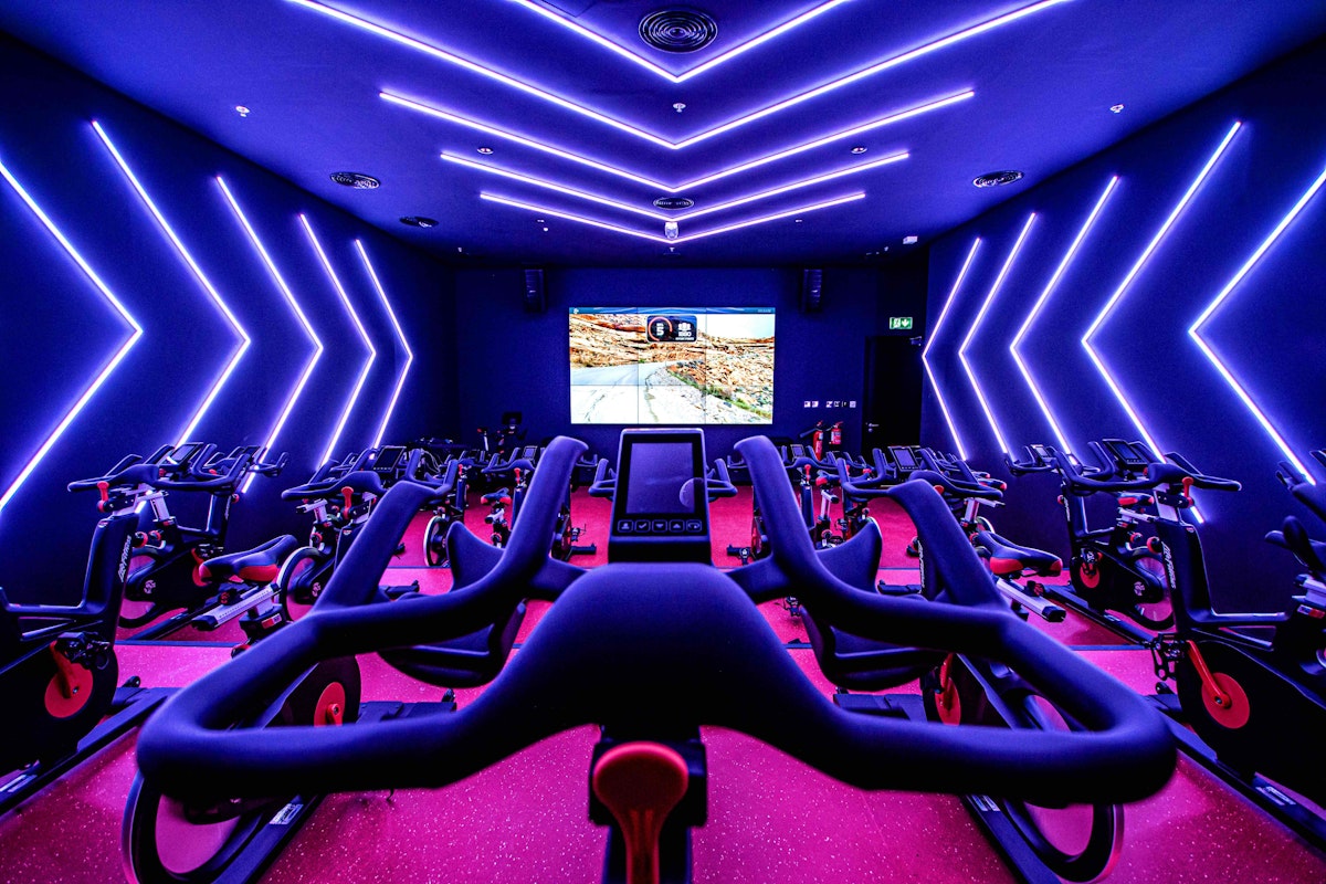 Spinning room with exercise bikes, neon lighting, and a screen showing a cycling map