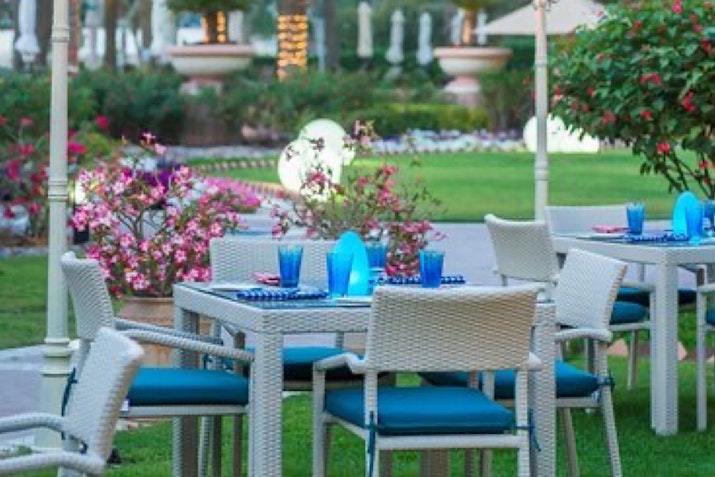 Al Raha Beach Hotel A beautifully arranged outdoor dining area with blue glasses, surrounded by vibrant flowers and greenery.