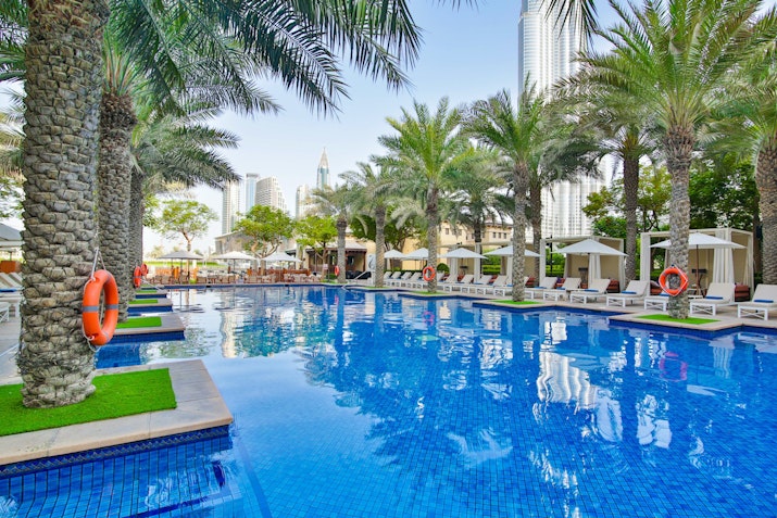 Hotel pool with palm trees, lounge chairs, and lifebuoys, surrounded by modern buildings
