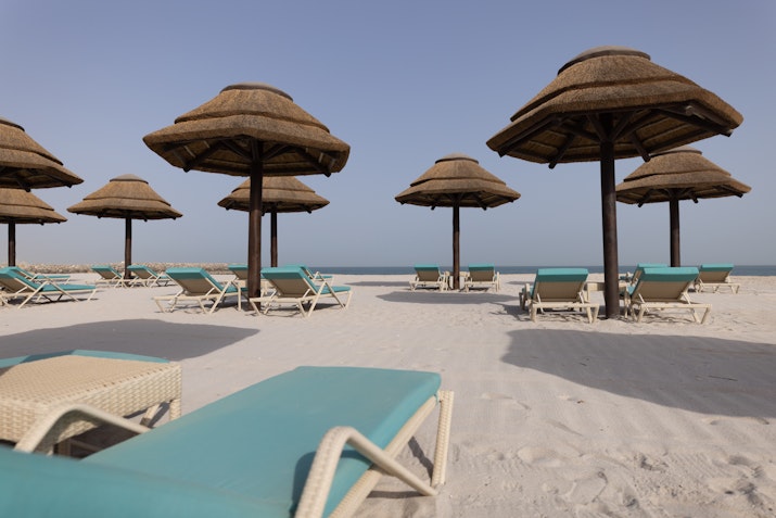 Beach lounge chairs and straw umbrellas arranged on a sandy beach, overlooking the calm sea.