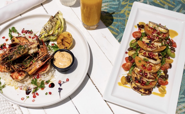 Two beautifully plated dishes featuring grilled prawns, rice, and a colorful salad with fresh vegetables and pomegranate seeds.
