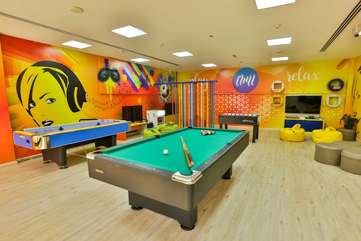 A vibrant game room featuring a pool table, air hockey table, colorful walls, and cozy seating.