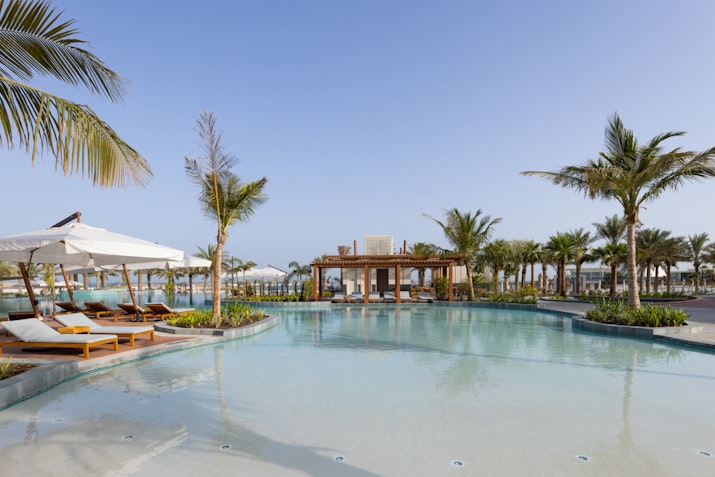 A clear pool with lounge chairs and palm trees around it.