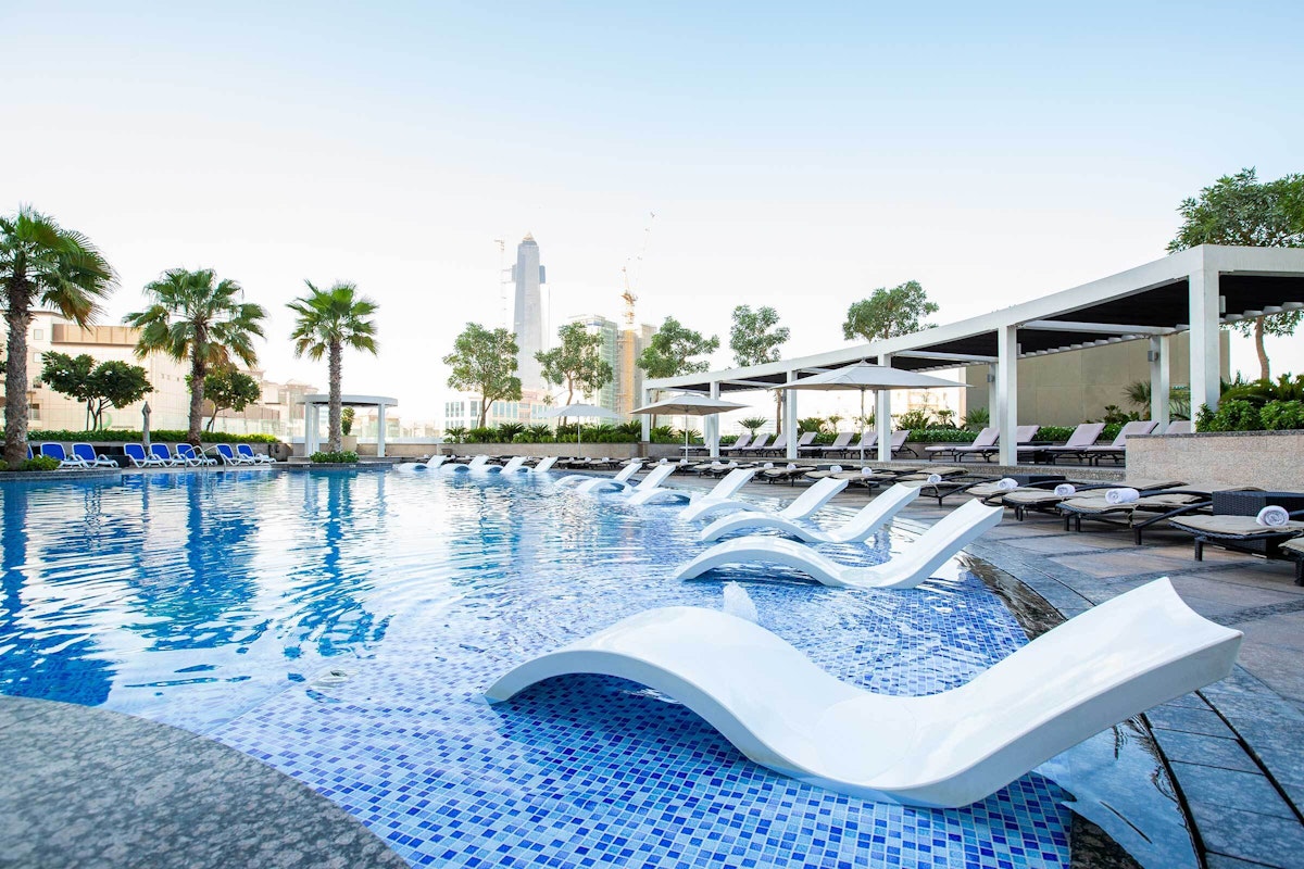 Modern poolside loungers beside a clear pool with a city skyline backdrop