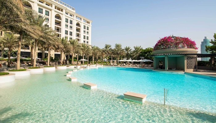 Palazzo Versace Dubai A serene pool area surrounded by palm trees and a luxury hotel, with clear blue water and a floral-decorated pavilion