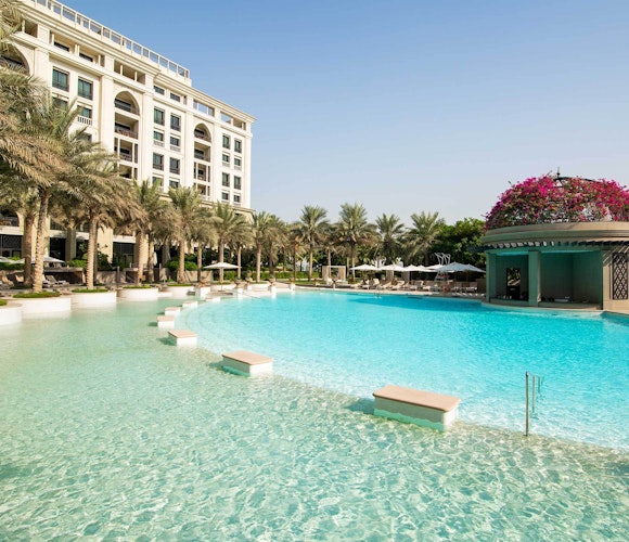 Palazzo Versace Dubai A serene pool area surrounded by palm trees and a luxury hotel, with clear blue water and a floral-decorated pavilion