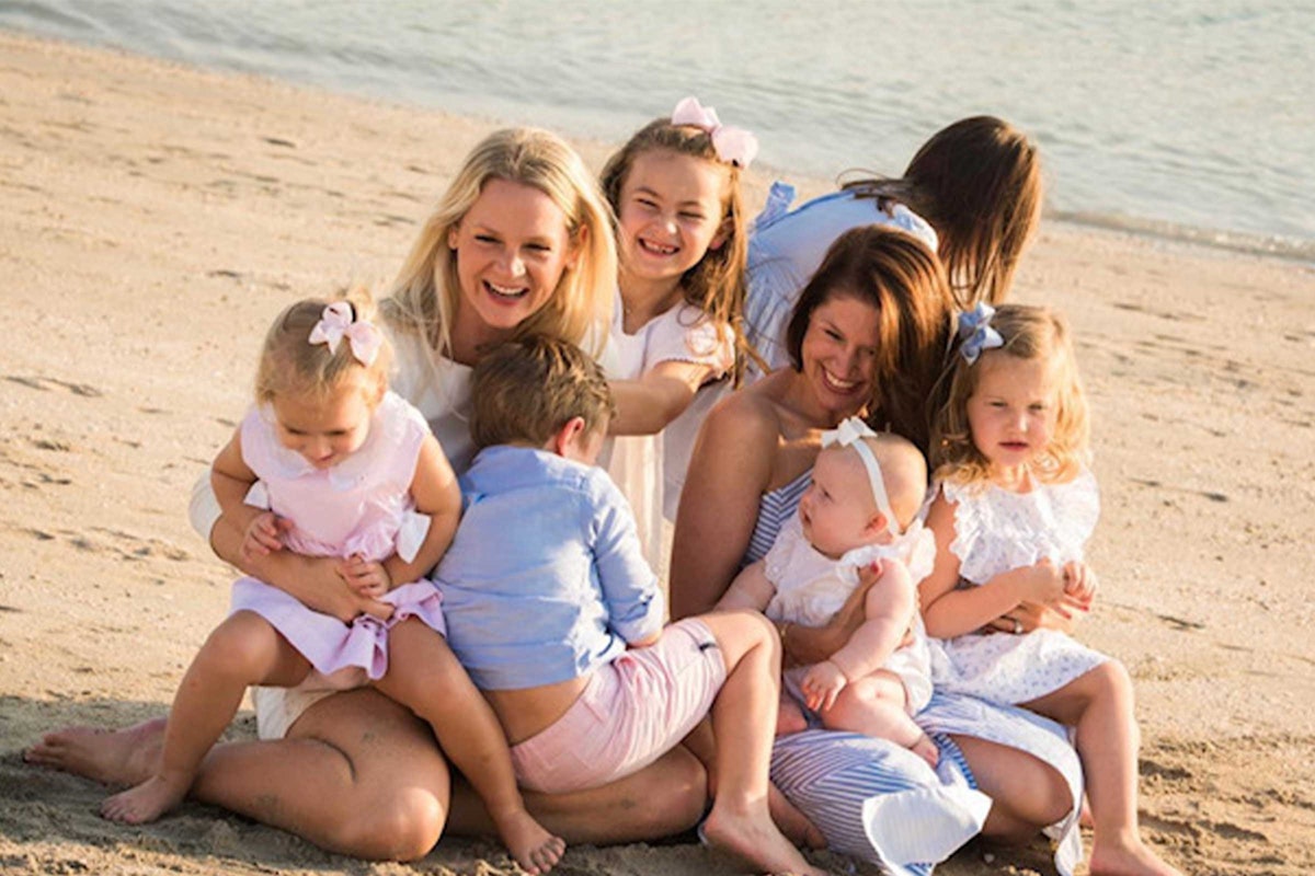A group of women and children sitting together on the beach, smiling and enjoying their time.