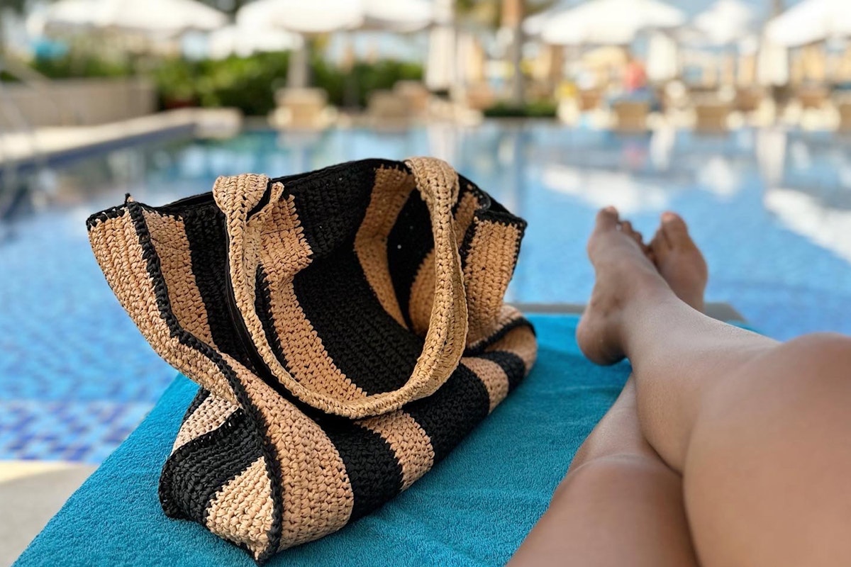 A beach bag resting next to a person's legs by the pool.