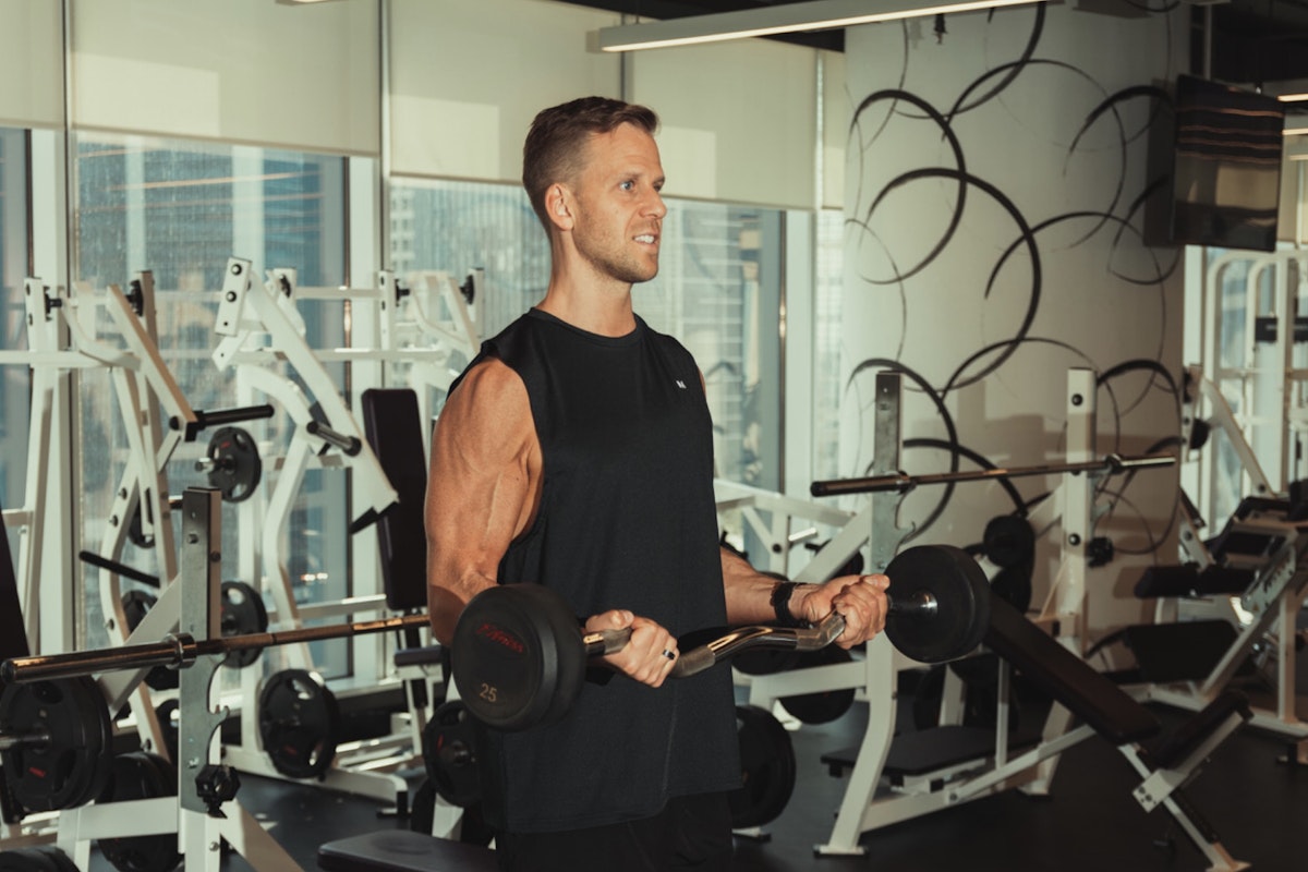Adam and Olivia McCubbin A person lifting a barbell in a gym, performing a bicep curl exercise.