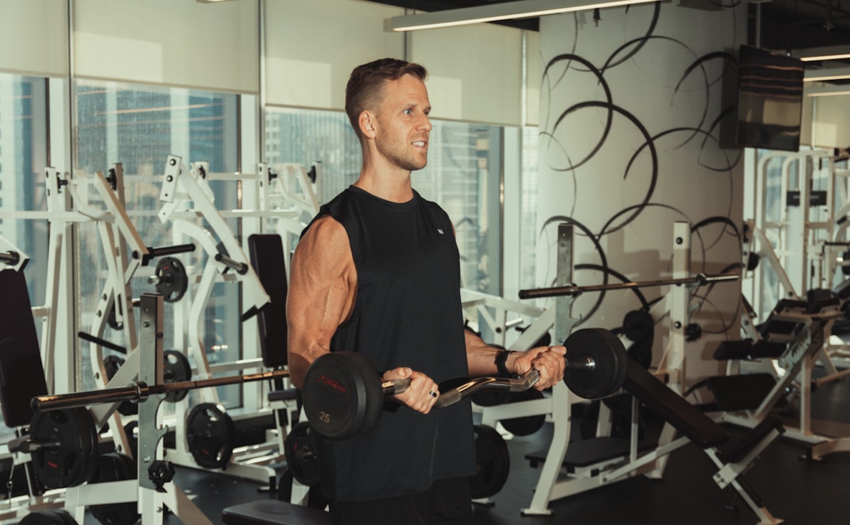 A person lifting a barbell in a gym, performing a bicep curl exercise.