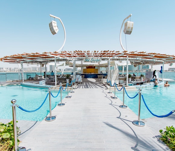 Café del Mar, Abu Dhabi Luxurious pool deck leading to a modern bar area with a wooden canopy, surrounded by water and lounging spaces.