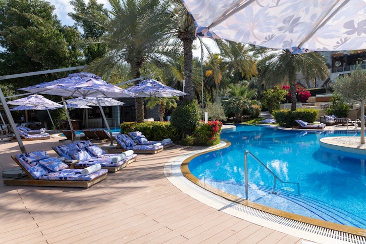 Poolside area with patterned loungers, umbrellas, and tropical landscaping.