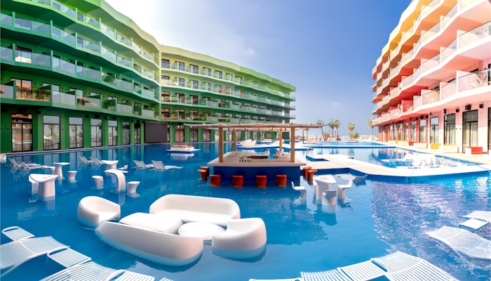 voco Monaco Dubai Colorful resort buildings surrounding a pool with in-water lounge seating