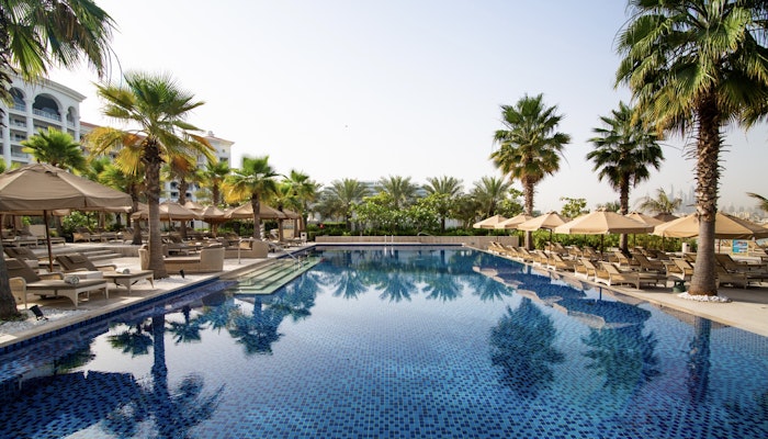 Waldorf Astoria Dubai Palm Jumeirah A pool surrounded by palm trees with lounge chairs beside it, under a clear blue sky.