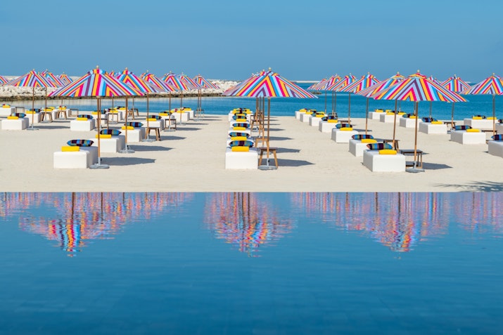A vibrant beach with colorful umbrellas and sunbeds, reflecting in the water.