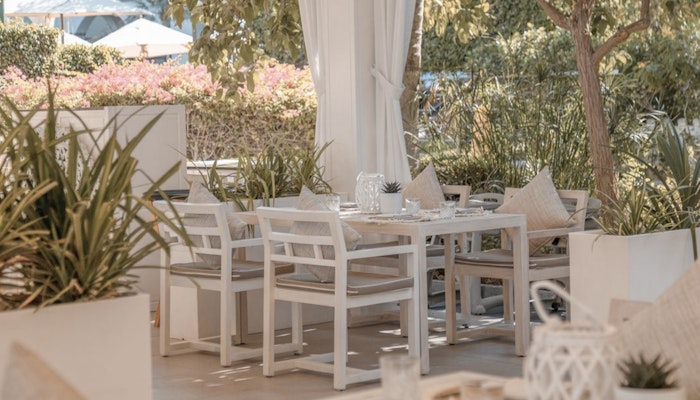 Zenzi Beach Outdoor dining area with white tables and chairs surrounded by greenery.