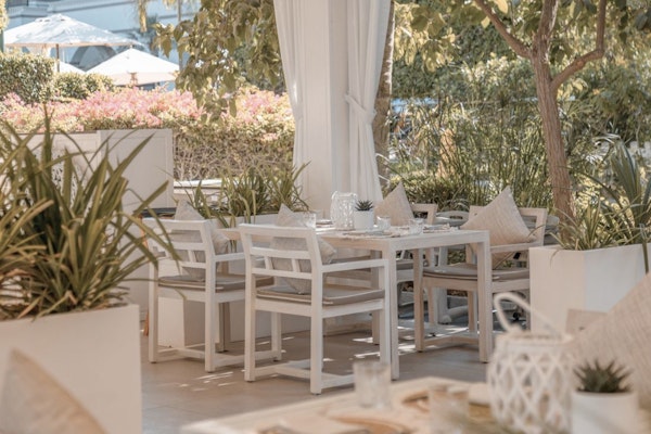 Outdoor dining area with white tables and chairs surrounded by greenery.
