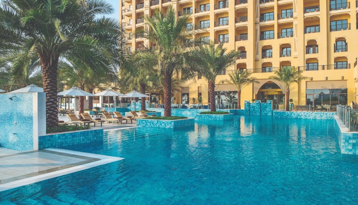 DoubleTree by Hilton Marjan Island A swimming pool surrounded by palm trees and sun loungers, with a hotel building in the background.