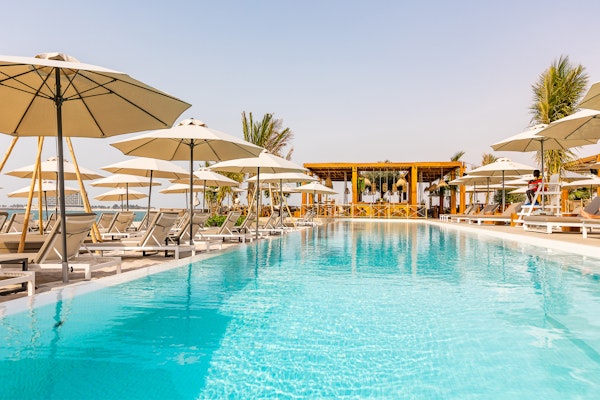 A serene poolside view featuring sun loungers and umbrellas, leading to a bar area with a tropical atmosphere.