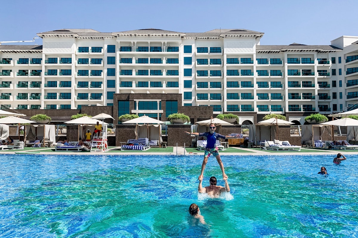A group of people enjoying a sunny day at a hotel pool, with one person performing a human pyramid stunt in the water