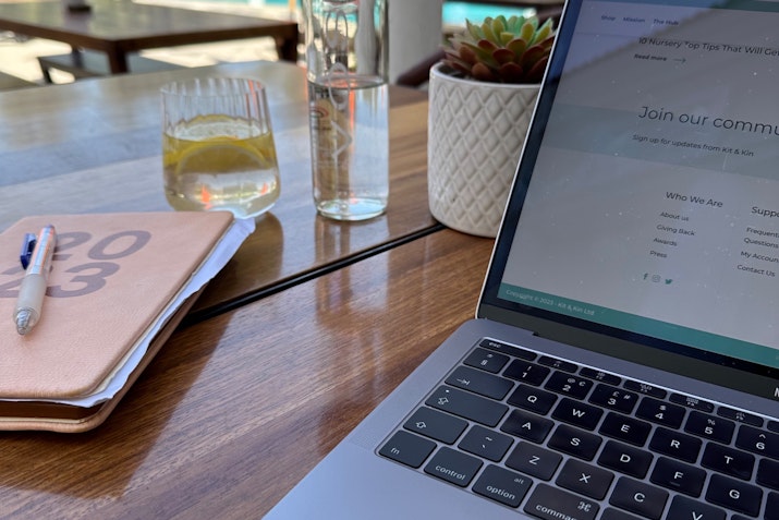 A desk setup with a MacBook, notebook, pens, and a drink.